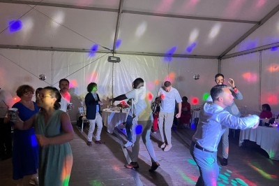 Des personnes dansent sous des lumières colorées dans une salle sous chapiteau lors d'un événement festif.