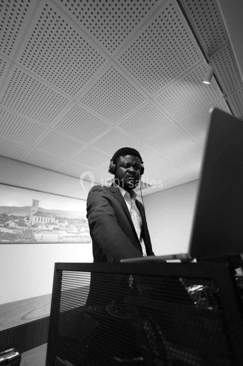 Un homme en costume utilise un ordinateur portable, portant un casque audio, dans une pièce au plafond perforé.