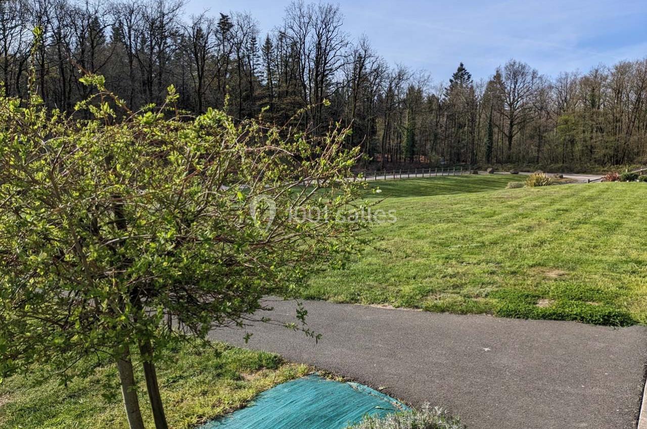 Allée bordée de pelouse et d'arbres dans un parc, avec un ciel dégagé en arrière-plan.
