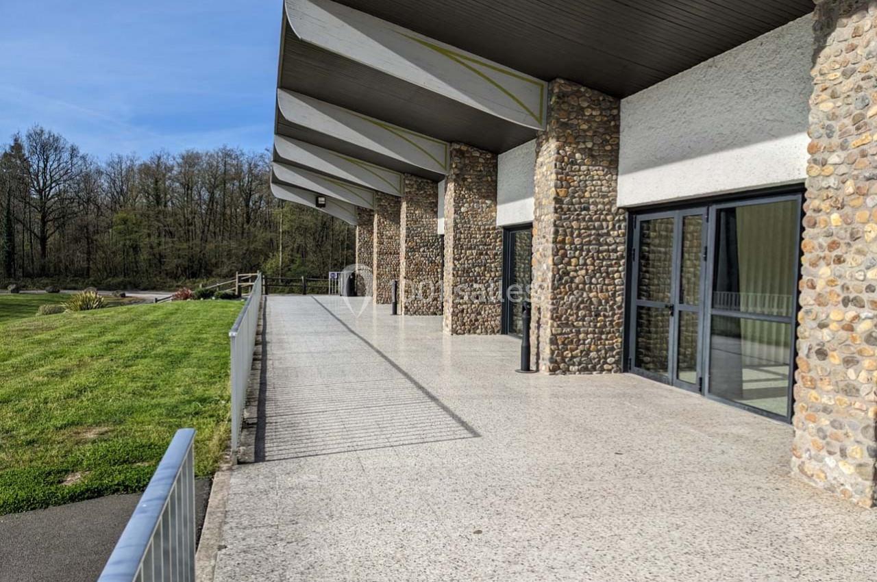 Terrasse en béton bordée de baies vitrées et de murs en pierre, donnant sur un espace vert et une forêt.