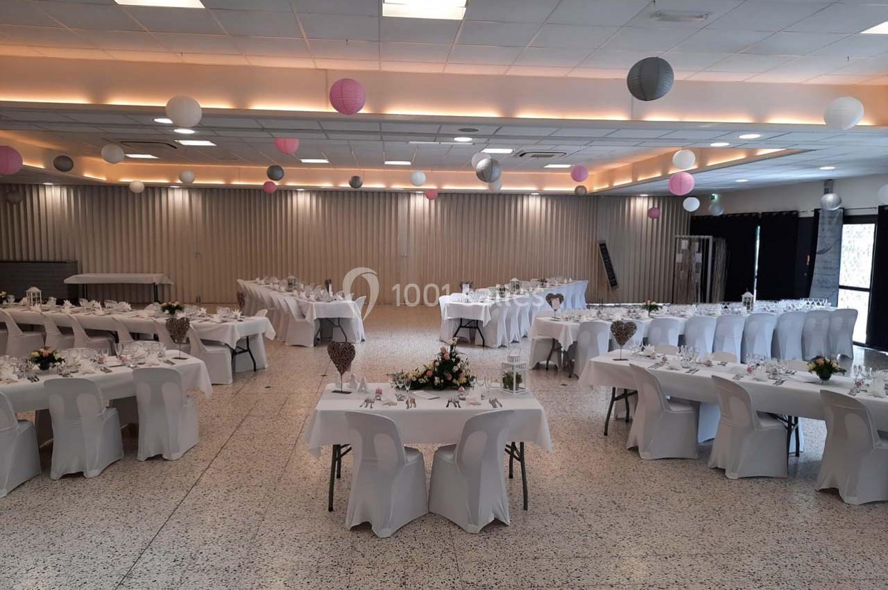 Salle de réception décorée avec des tables dressées, nappes blanches et suspensions colorées au plafond.