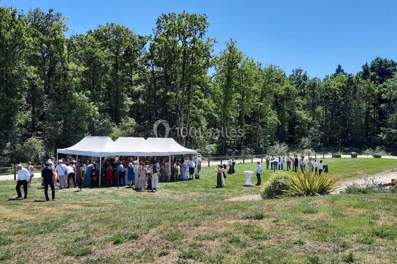Groupe de personnes rassemblées sous des tentes blanches dans un espace extérieur verdoyant par une journée ensoleillée.