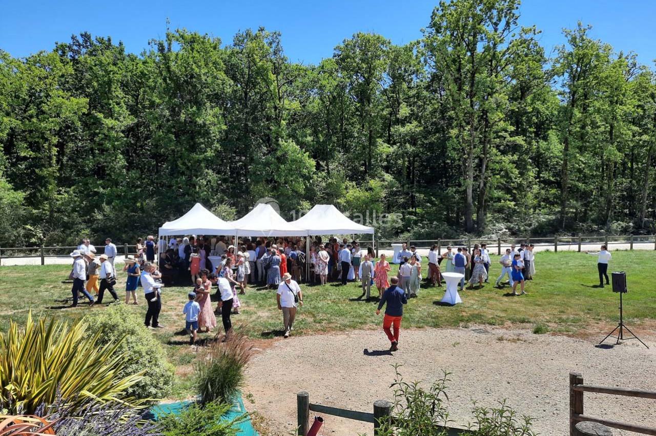 Groupe de personnes rassemblées sous des tentes blanches dans un espace extérieur verdoyant par une journée ensoleillée.