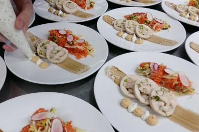 Assiettes dressées avec des roulés de volaille, légumes râpés et décorations de sauce, en préparation en cuisine.