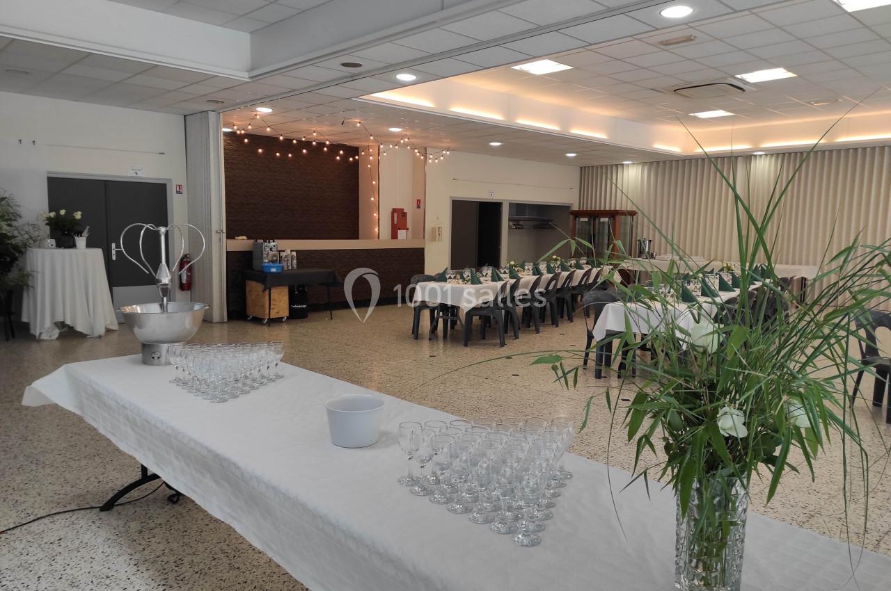 Salle de réception lumineuse avec tables dressées, plantes décoratives et espace pour boissons sur une table blanche.