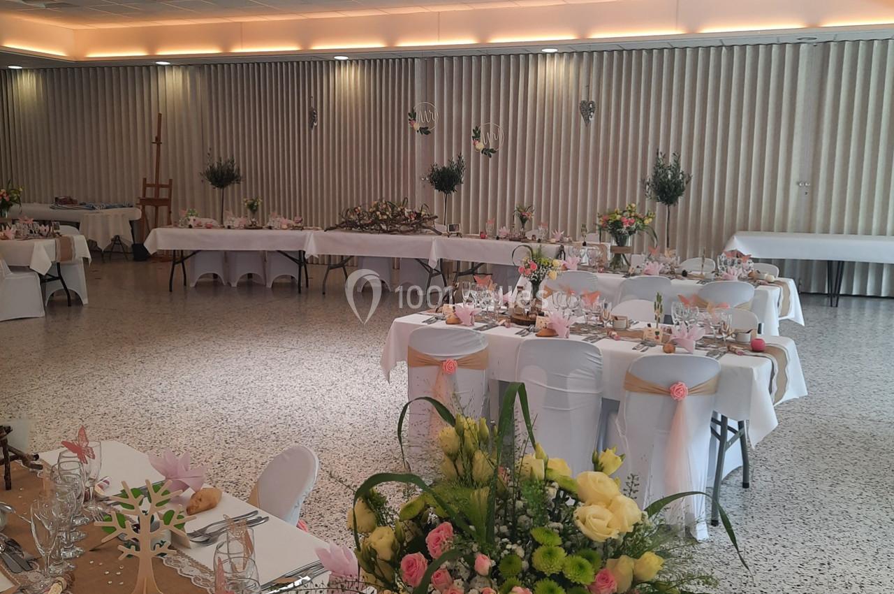 Salle de réception décorée pour un événement, avec tables dressées, fleurs et éclairage tamisé.