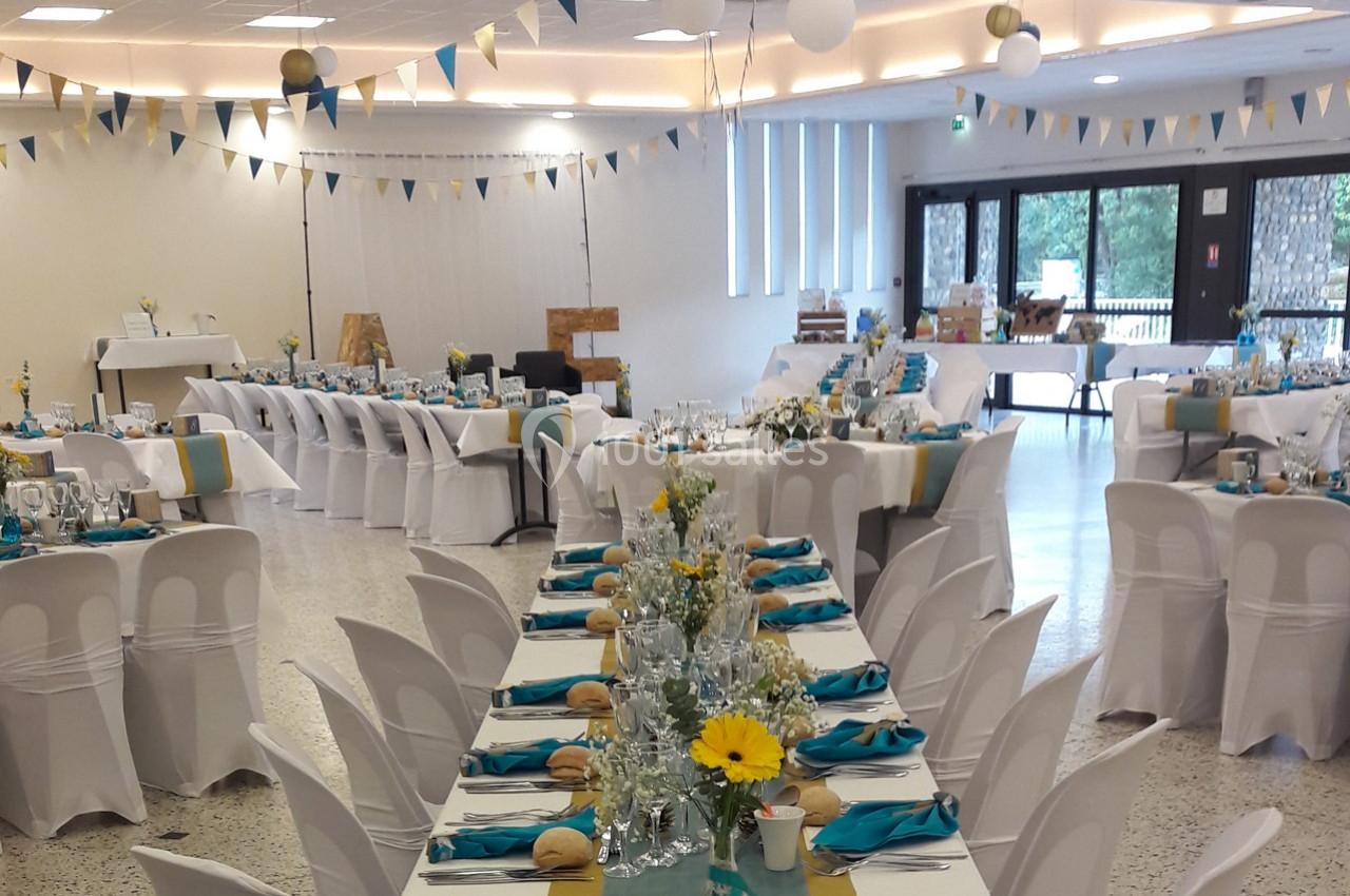 Salle de réception décorée pour un événement, avec tables dressées, nappes blanches et accents turquoise et jaunes.