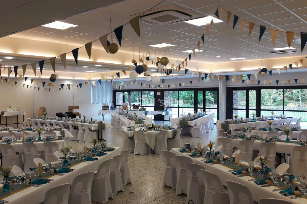 Salle de réception décorée avec des guirlandes et des tables dressées pour un événement festif.