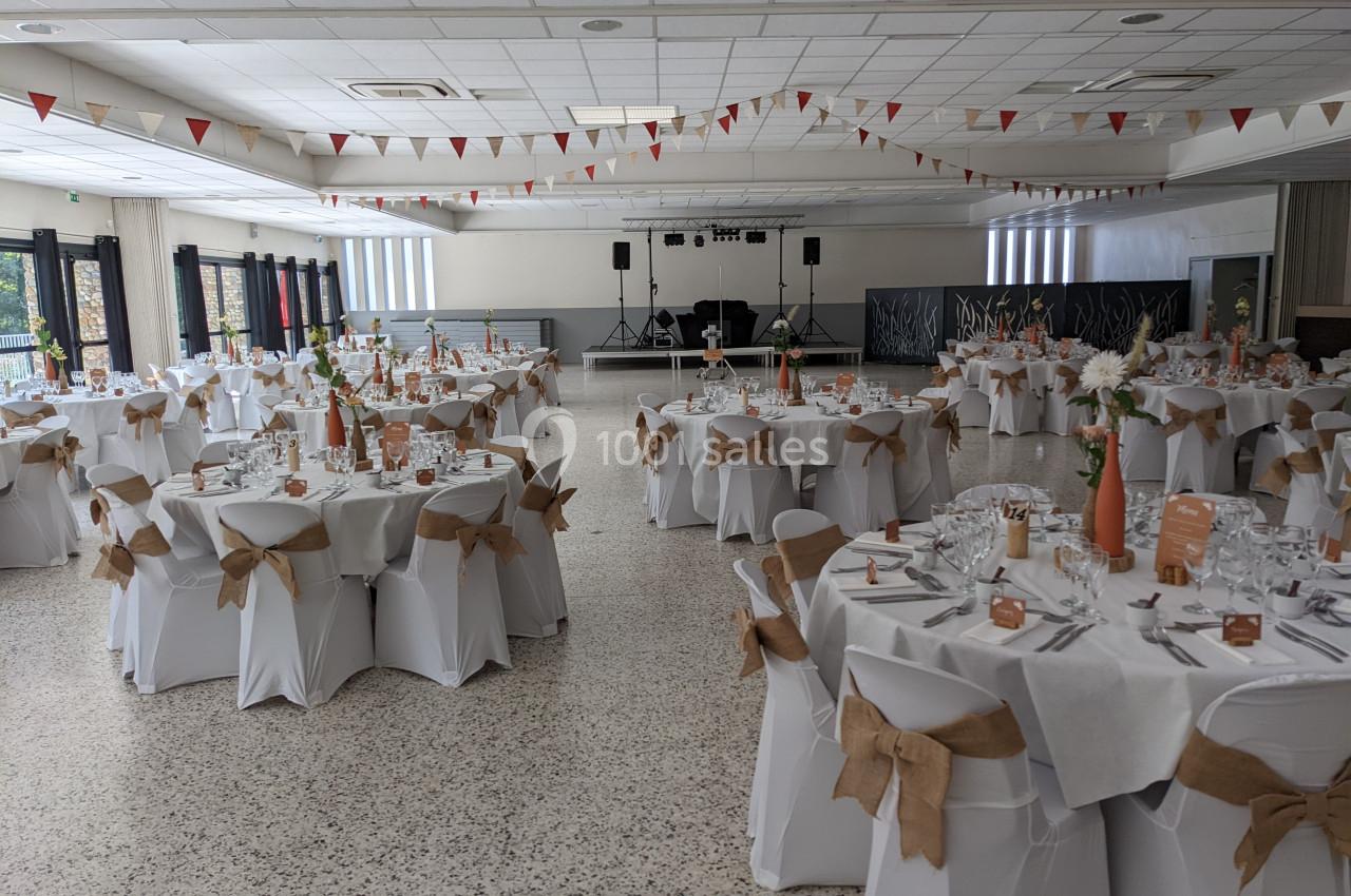 Salle de réception décorée avec des tables rondes dressées, nappes blanches et chaises ornées de nœuds en toile de jute.