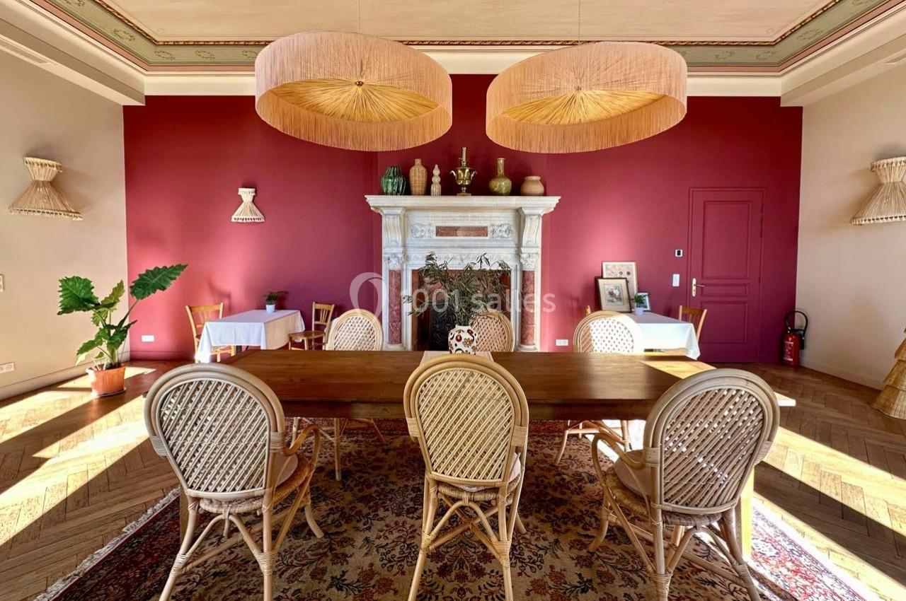 Salle à manger avec table en bois, chaises en rotin, cheminée décorative et murs rouges.