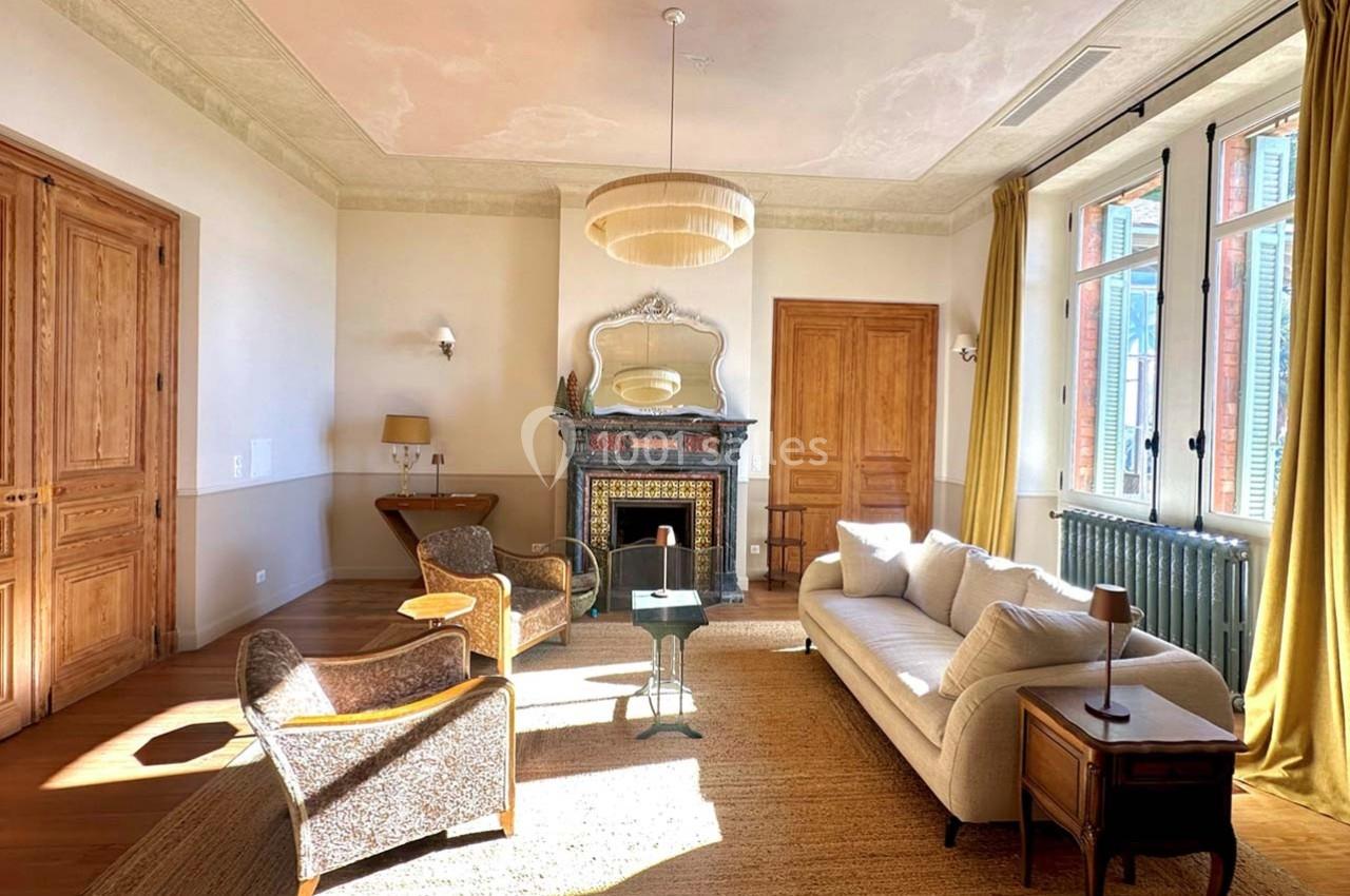 Salon lumineux avec cheminée décorative, mobilier élégant, grandes fenêtres et parquet en bois clair.