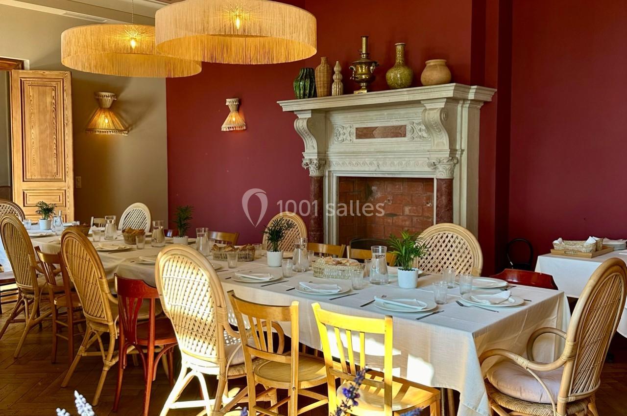 Salle à manger avec murs rouges, cheminée décorative, tables dressées et chaises en bois, éclairée par des suspensions en…