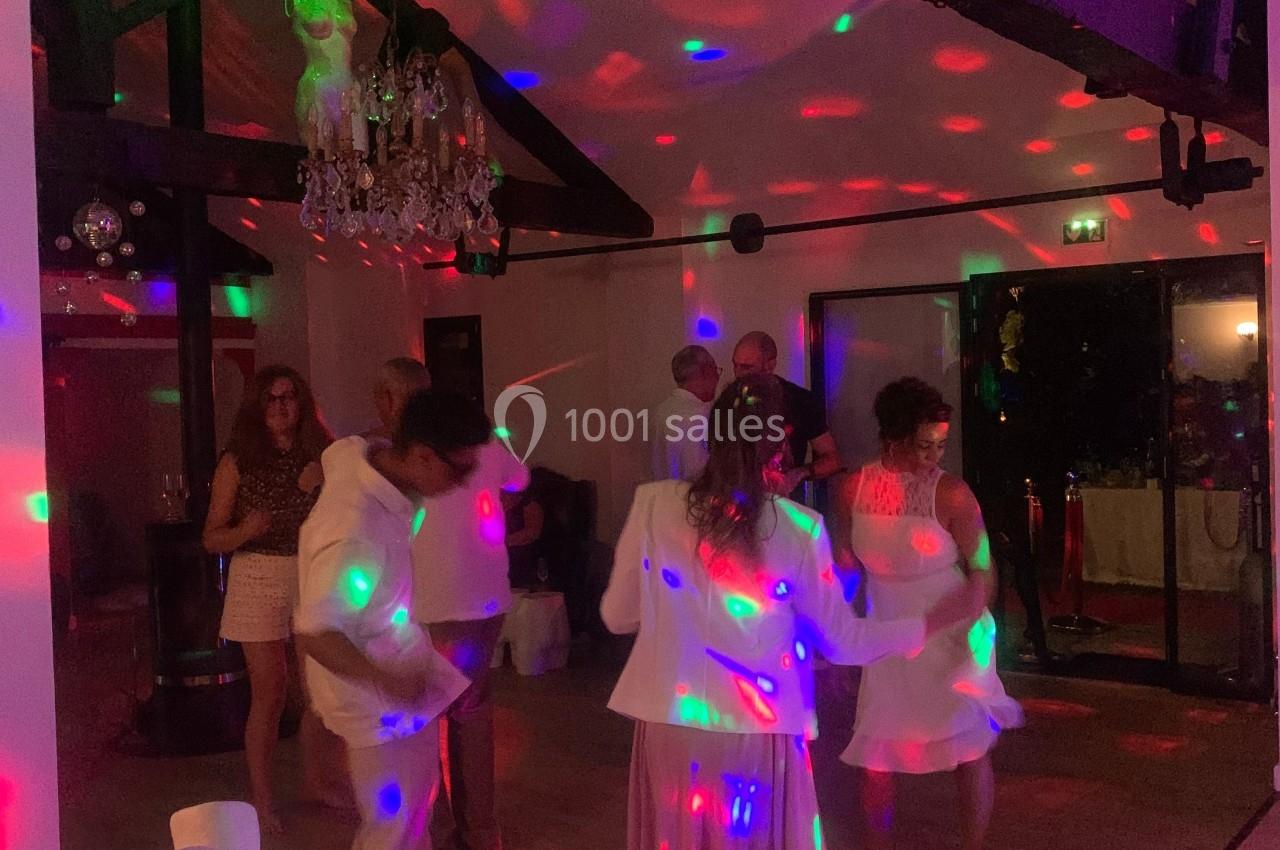 Des personnes dansent dans une salle éclairée par des lumières colorées, avec des poutres apparentes au plafond.