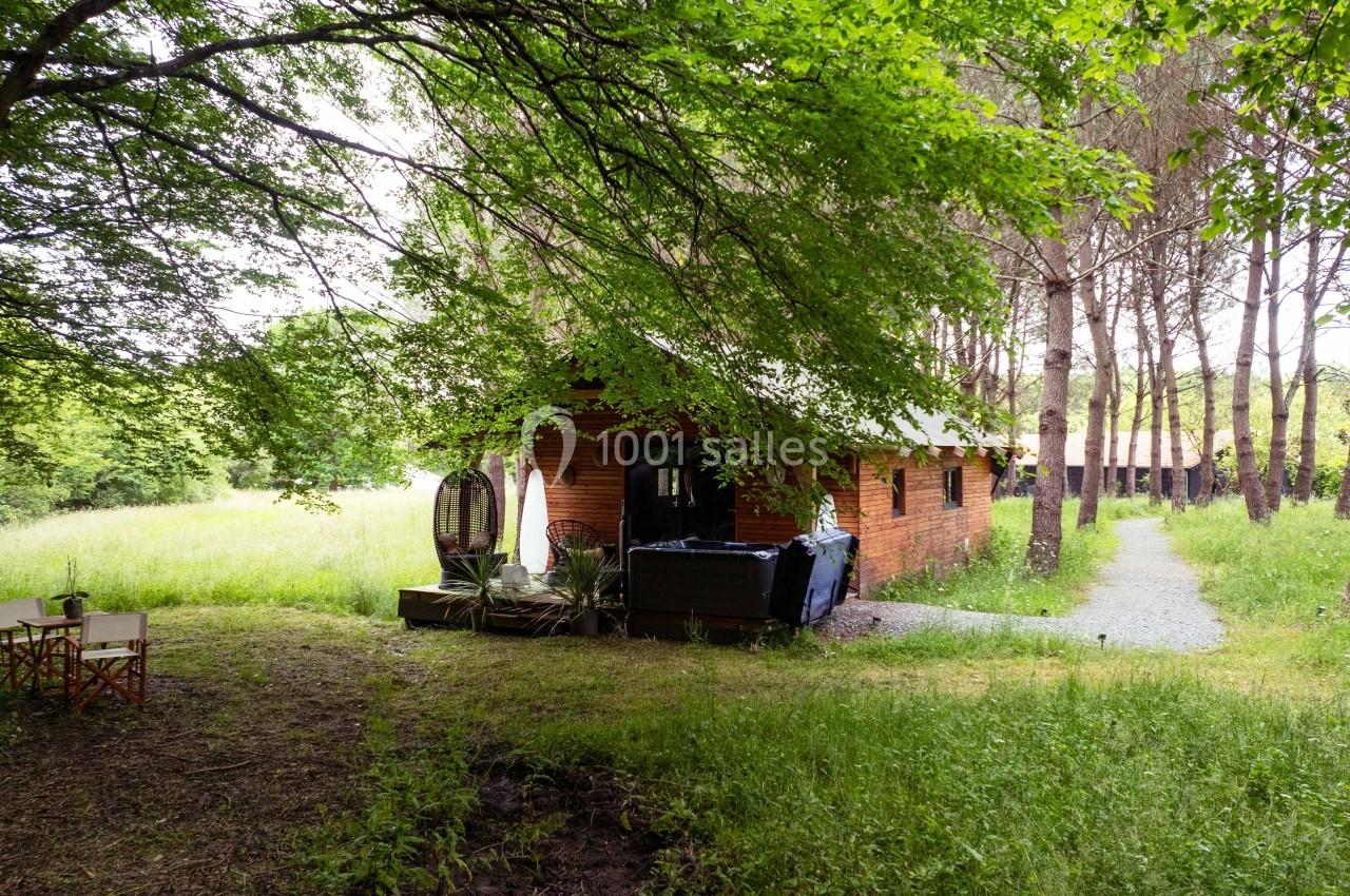 Cabane en bois entourée d'arbres et de verdure, avec un chemin menant à une clairière.