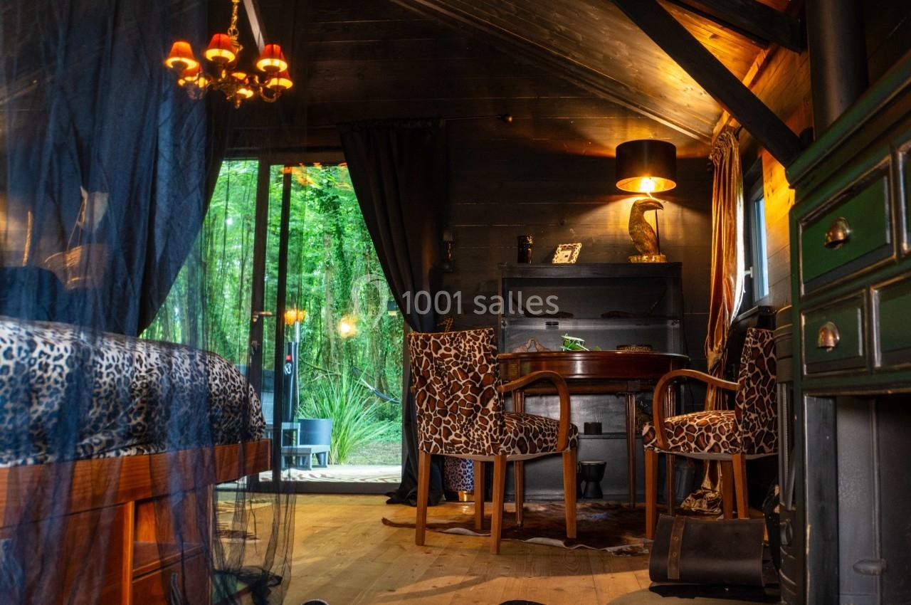 Intérieur d'une cabane en bois avec mobilier en bois sombre, chaises à motifs, et vue sur une forêt par une porte vitrée.