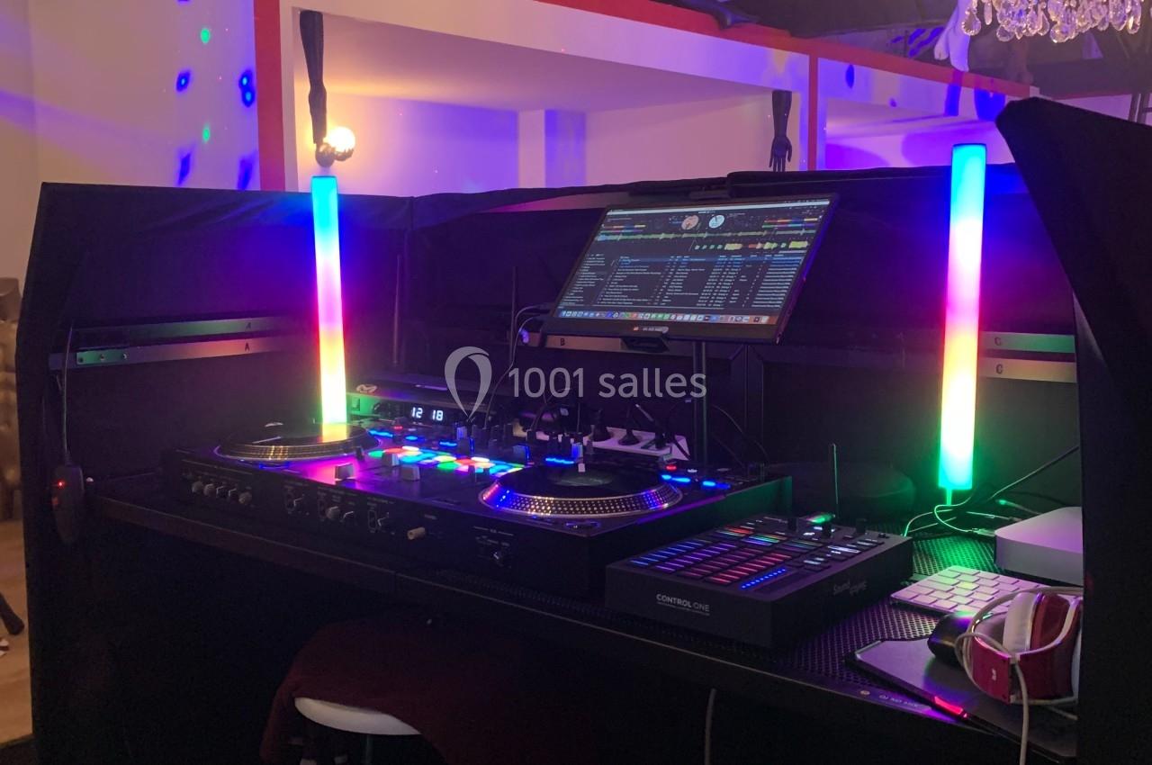 Poste de DJ avec platines, table de mixage, écran et éclairages LED colorés dans une pièce au plafond avec poutres…