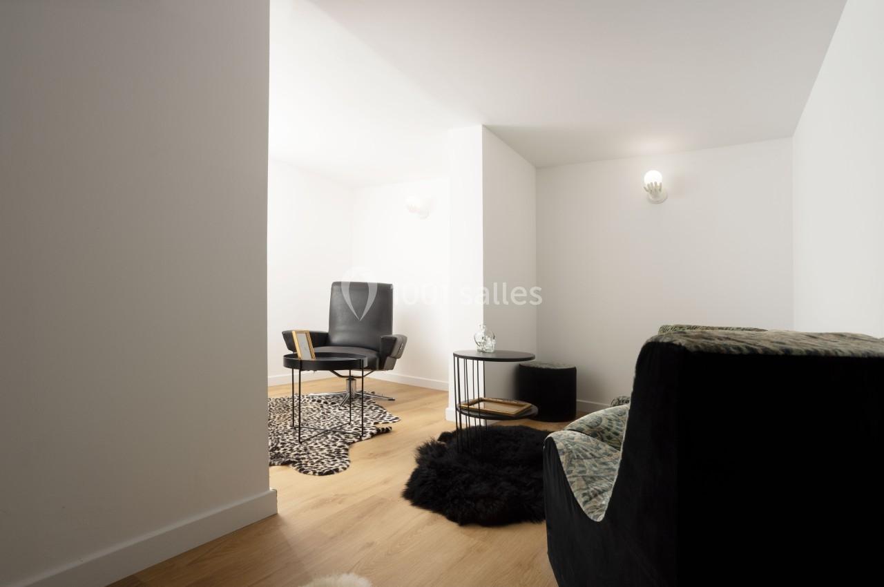 Espace intérieur minimaliste avec fauteuil noir, table basse ronde, tapis à motifs et sol en bois clair.