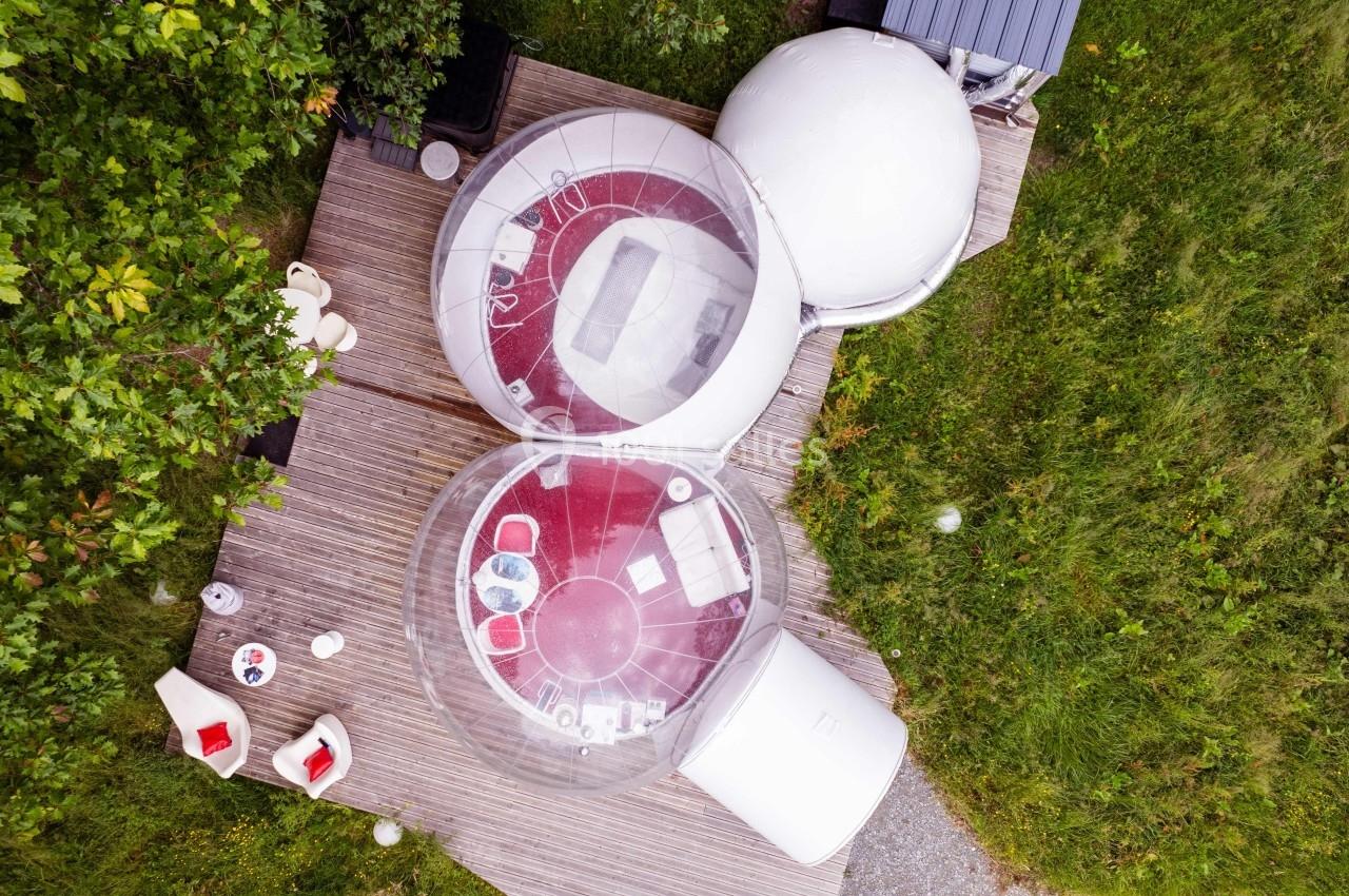 Vue aérienne de bulles transparentes aménagées avec mobilier rouge, installées sur une terrasse en bois entourée de verdure.