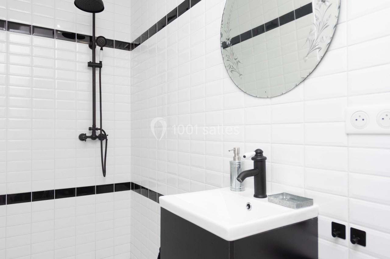 Salle de bain moderne avec carrelage blanc, douche noire, miroir rond et meuble vasque noir.