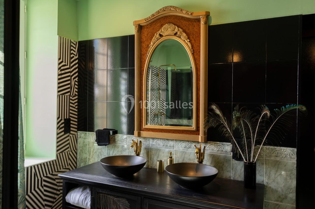 Salle de bain avec un grand miroir doré, deux vasques noires, robinetterie dorée et décoration moderne.