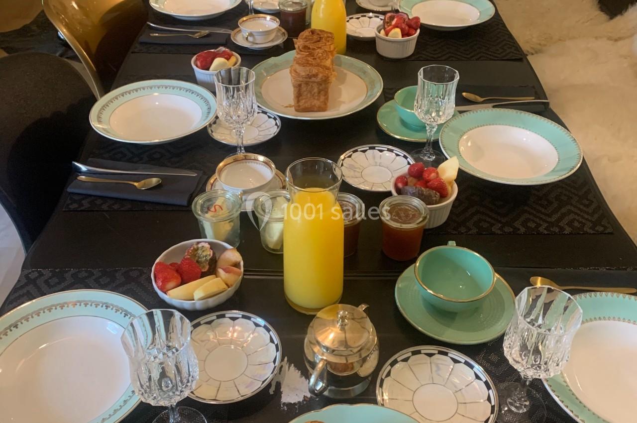 Table dressée pour un petit-déjeuner avec viennoiseries, fruits, jus d'orange et vaisselle élégante.