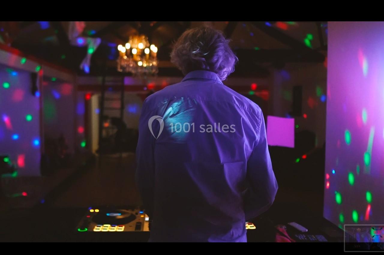 Un DJ de dos mixe dans une salle sombre illuminée par des lumières colorées et un lustre au plafond.