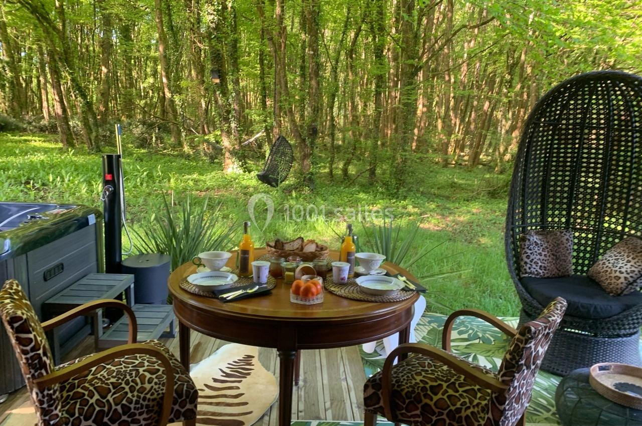 Table dressée pour un petit-déjeuner en plein air sur une terrasse boisée, entourée de verdure et d'un spa.