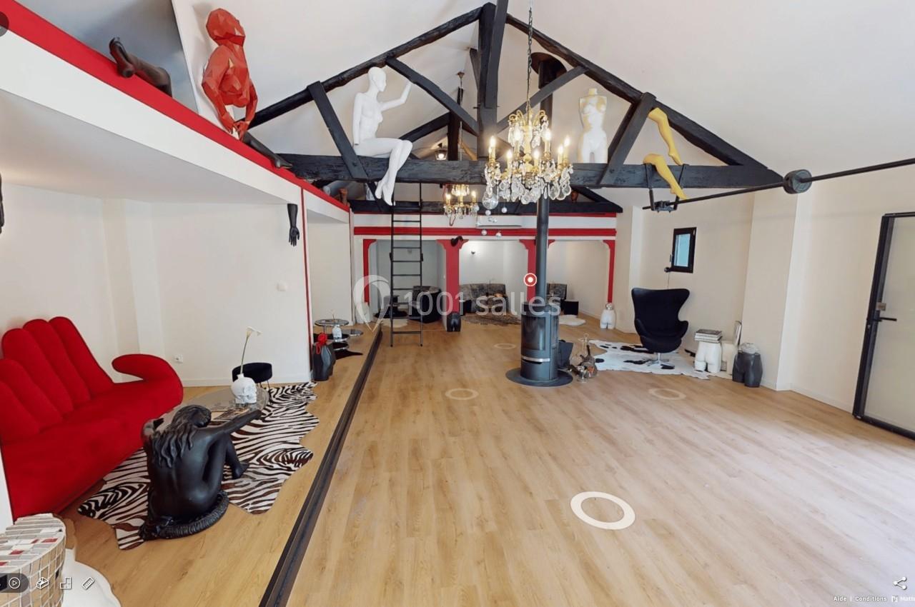 Salle spacieuse avec parquet, poutres apparentes, mobilier éclectique et sculptures colorées suspendues.