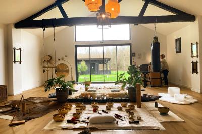 Extérieur d'une maison avec façade sombre, mobilier en osier et peaux, entourée de verdure et de bambous.