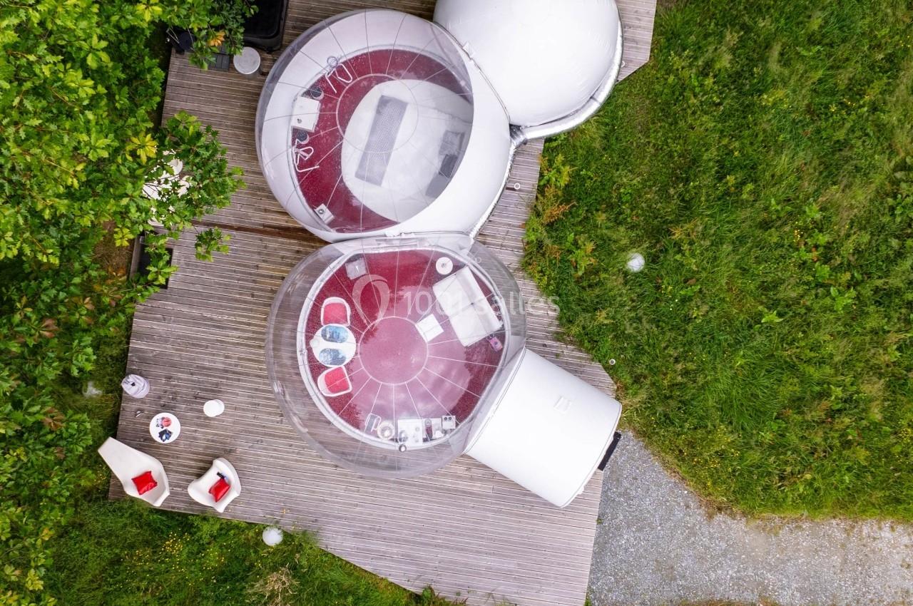 Vue aérienne de deux bulles transparentes aménagées sur une terrasse en bois, entourées de verdure.