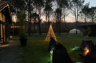 Extérieur d'une maison avec façade sombre, mobilier en osier et peaux, entourée de verdure et de bambous.