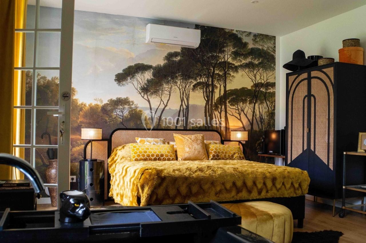Chambre lumineuse avec lit double, décoration jaune et noire, mur orné d'une fresque de paysage forestier.