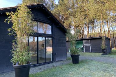 Extérieur d'une maison avec façade sombre, mobilier en osier et peaux, entourée de verdure et de bambous.