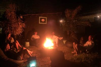 Extérieur d'une maison avec façade sombre, mobilier en osier et peaux, entourée de verdure et de bambous.
