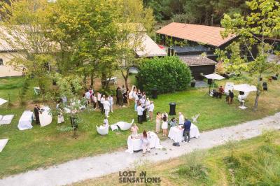 Extérieur d'une maison avec façade sombre, mobilier en osier et peaux, entourée de verdure et de bambous.
