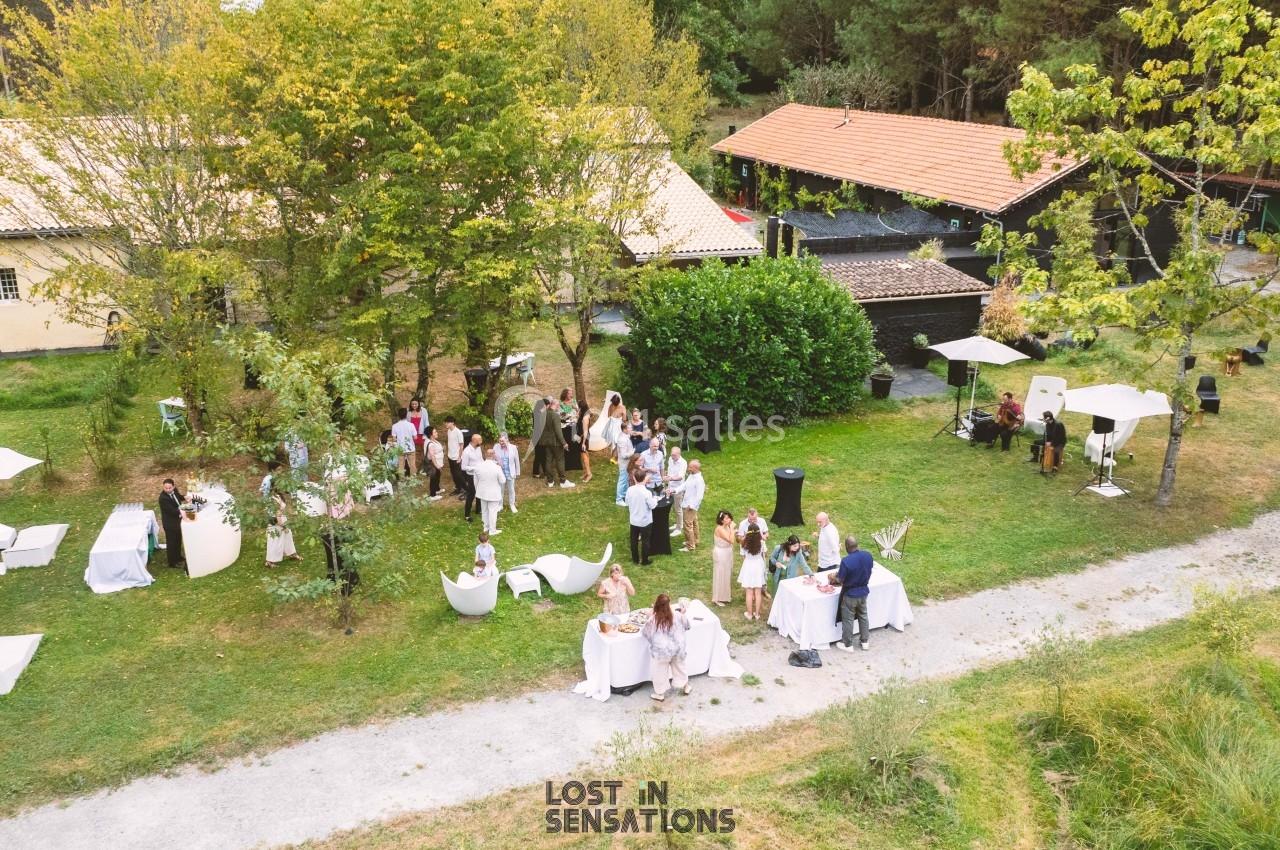 Vue aérienne d'un rassemblement en plein air avec des invités autour de tables dans un cadre verdoyant près de bâtiments.