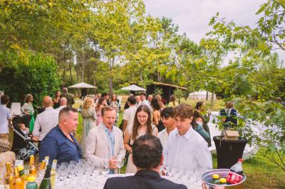 Extérieur d'une maison avec façade sombre, mobilier en osier et peaux, entourée de verdure et de bambous.