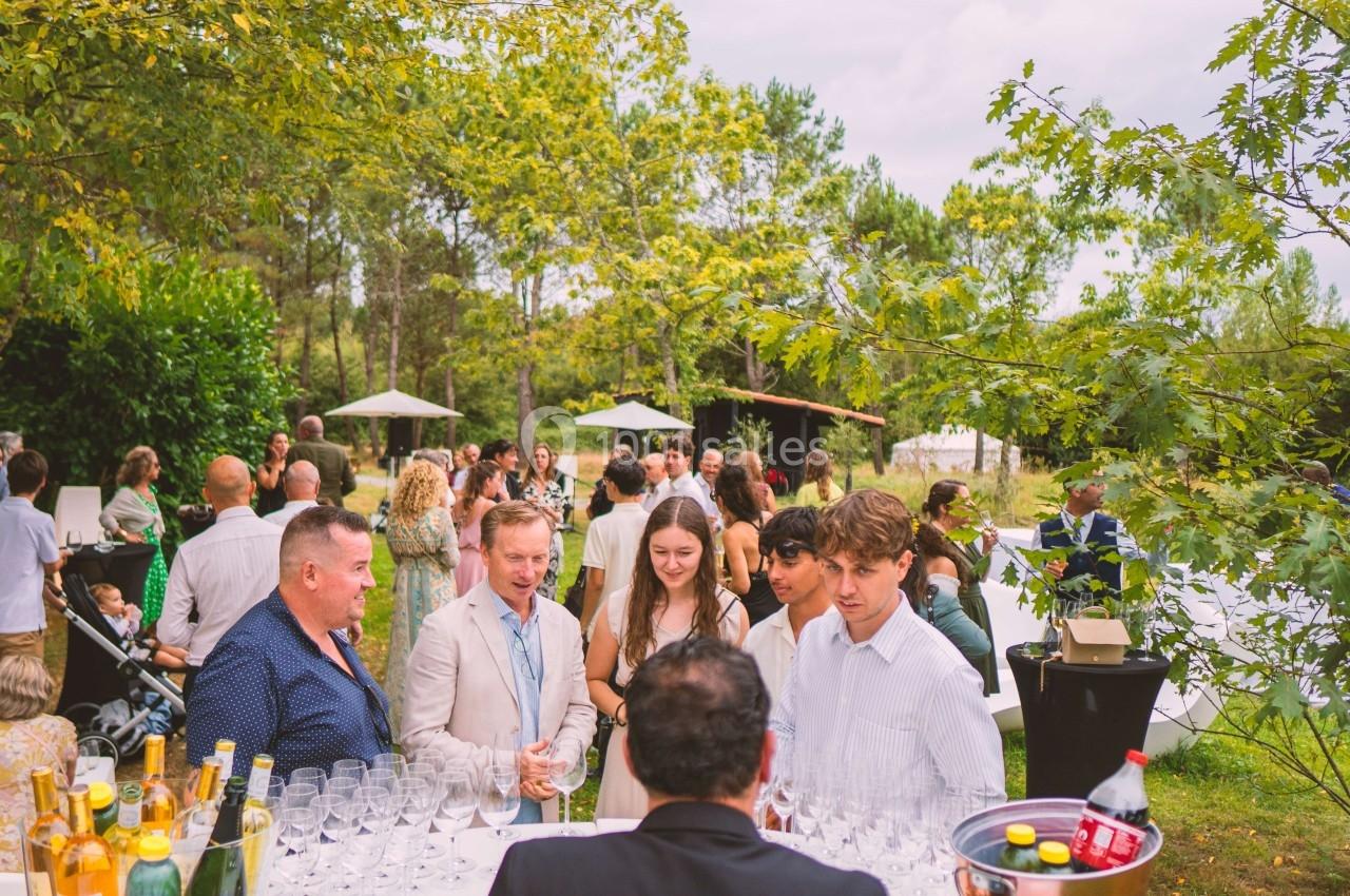 Groupe de personnes discutant lors d'un événement en plein air, entouré de verdure et de tables dressées.