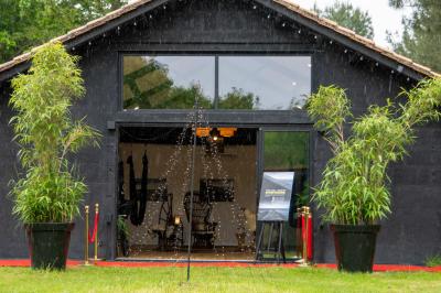 Extérieur d'une maison avec façade sombre, mobilier en osier et peaux, entourée de verdure et de bambous.