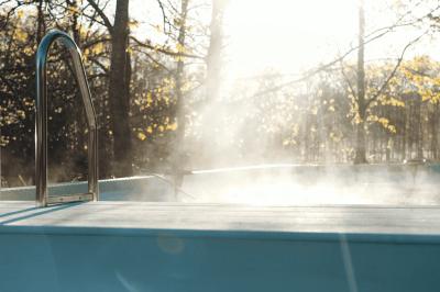 Extérieur d'une maison avec façade sombre, mobilier en osier et peaux, entourée de verdure et de bambous.