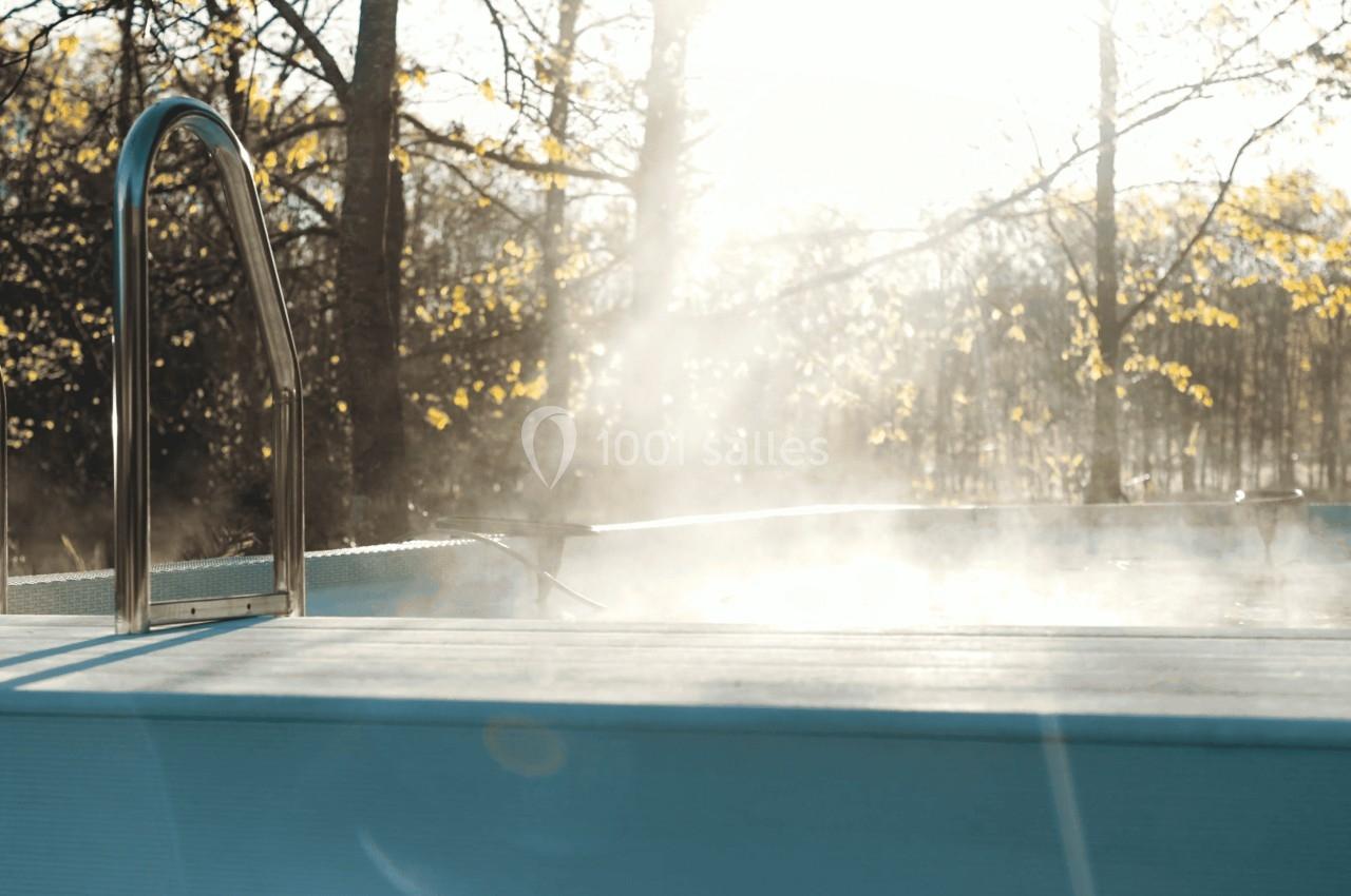 Piscine extérieure avec vapeur s'élevant dans l'air, entourée d'arbres illuminés par une lumière douce.