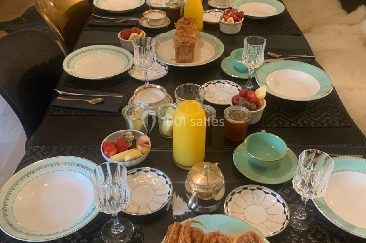 Table dressée pour un petit-déjeuner avec viennoiseries, fruits, jus d'orange et vaisselle élégante.