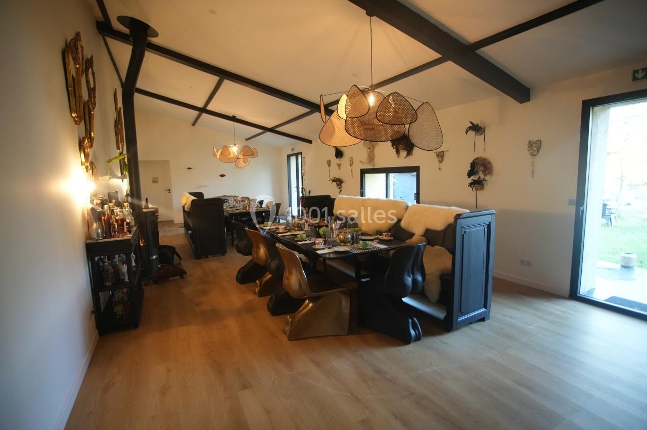 Salle à manger moderne avec table dressée, chaises design, luminaires suspendus et vue sur un jardin à travers une porte…