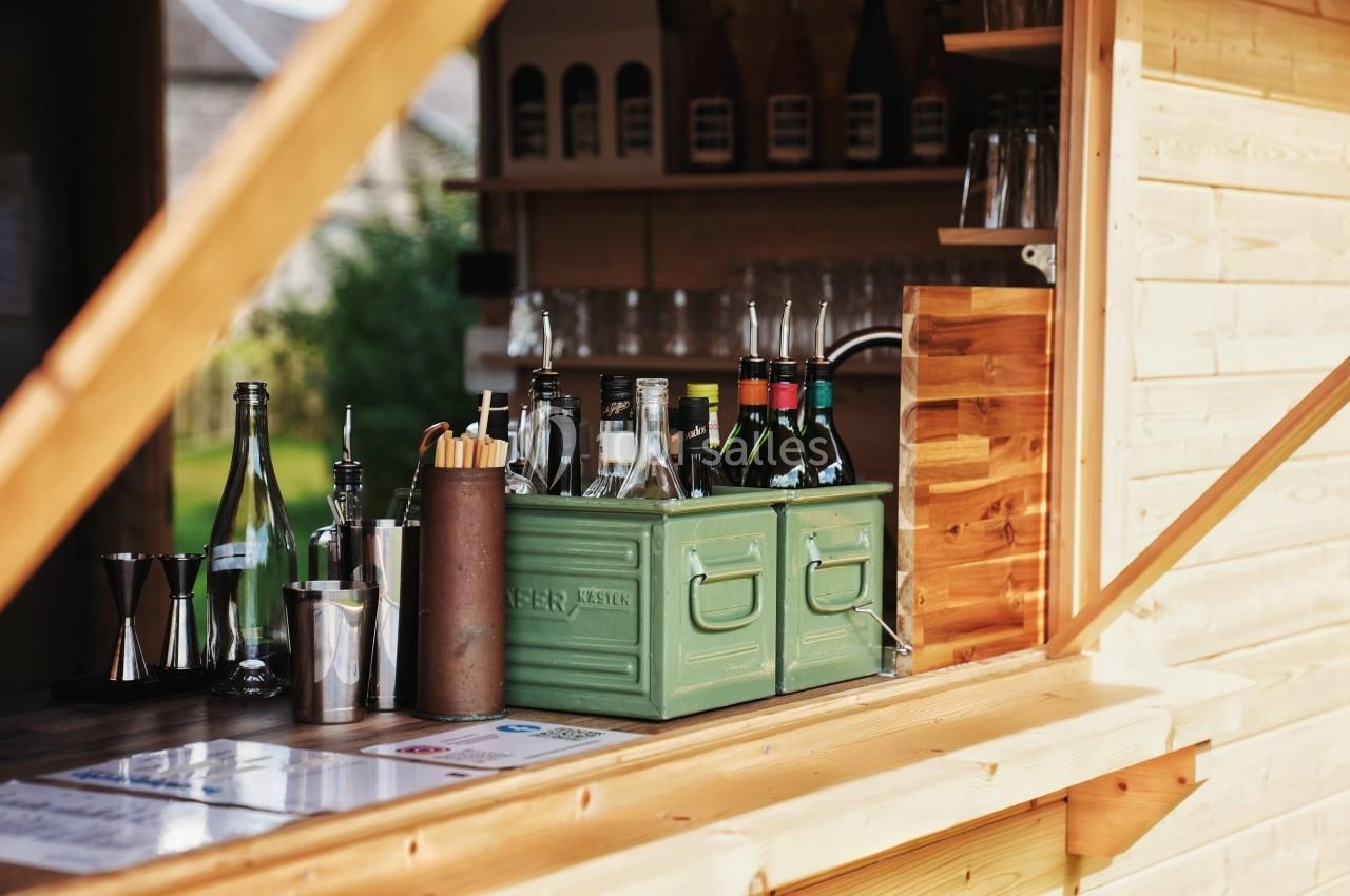 Comptoir en bois d'un bar extérieur avec bouteilles, verres et accessoires de préparation de boissons.