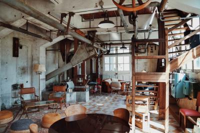 Espace lumineux avec plafond en bois, grandes fenêtres, mobilier varié et ambiance de loft industriel.