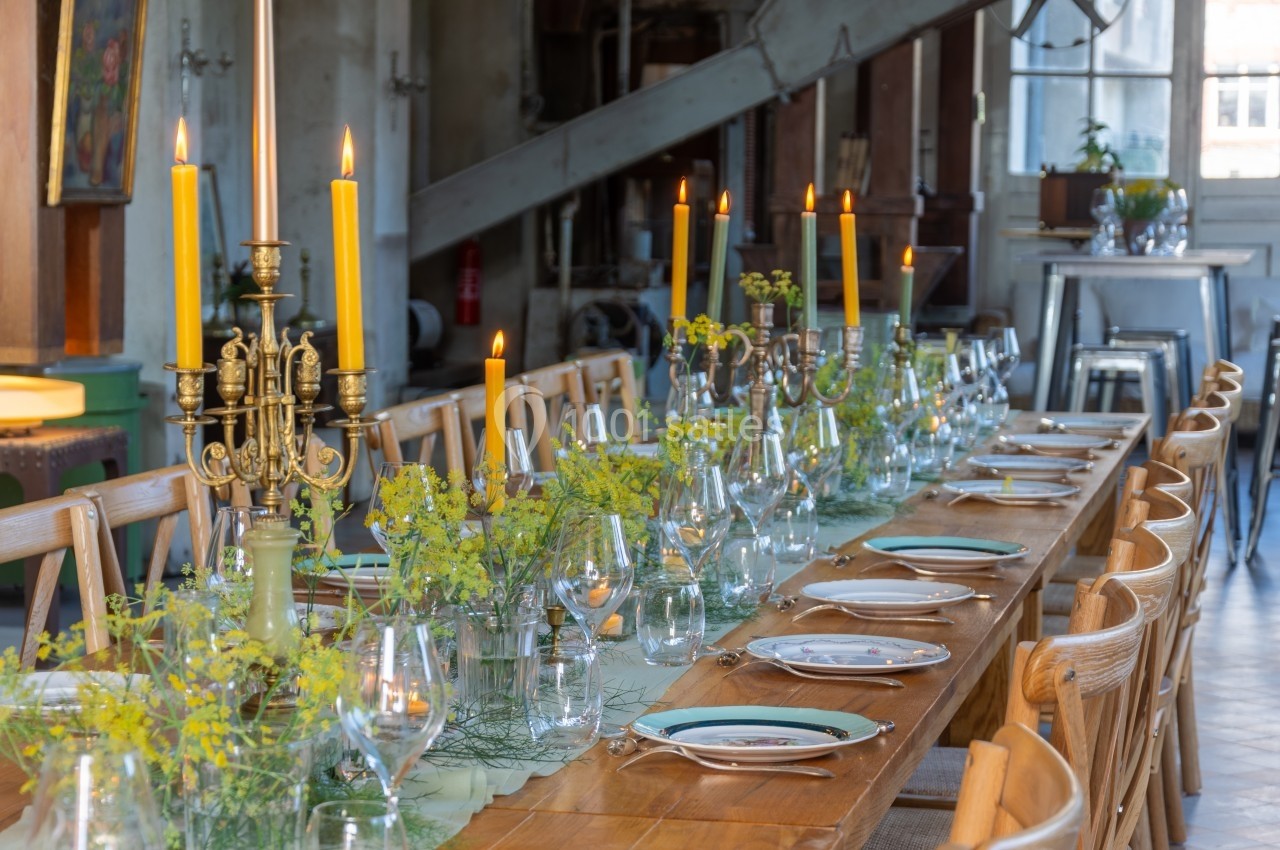 Table en bois dressée avec des chandeliers, des bougies allumées, de la vaisselle et des décorations florales jaunes.