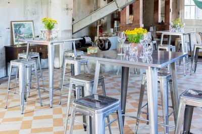 Espace lumineux avec plafond en bois, grandes fenêtres, mobilier varié et ambiance de loft industriel.