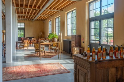 Espace lumineux avec plafond en bois, grandes fenêtres, mobilier varié et ambiance de loft industriel.