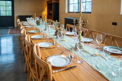 Table en bois dressée pour un repas, avec assiettes, verres, couverts, bougies et décoration centrale élégante.