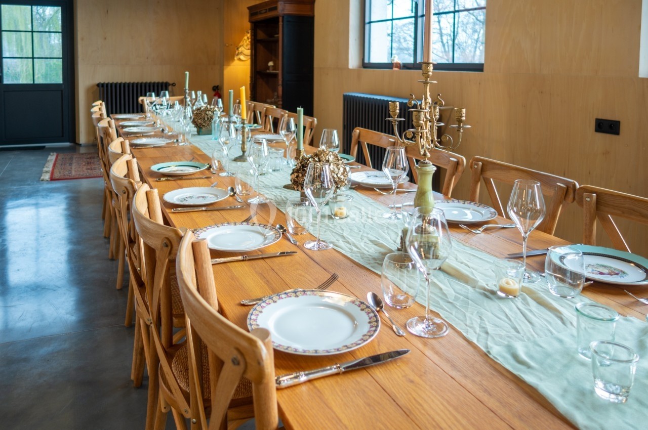 Table en bois dressée pour un repas, avec assiettes, verres, couverts, bougies et décoration centrale élégante.
